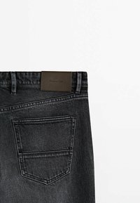 Vue arrière d'un jean en denim noir avec une poche arrière visible et une étiquette de marque en cuir marron sur la ceinture.