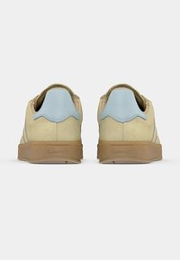 Αθλητικά παπούτσια από σουέντ σε ανοιχτό μπεζ χρώμα με μπλε δερμάτινο ταμπελάκι στη φτέρνα. Διαθέτουν υφή στη σόλα από καουτσούκ και διακριτικό λογότυπο στη φτέρνα.