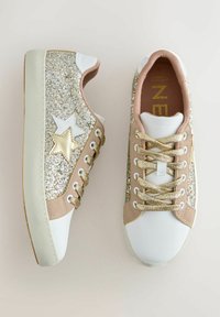 Baltie sporta apavi ar zelta un krēmkrāsas akcentiem; satur mirdzošas sānu paneļu un zvaigžņu motīvus, apaļas stingras auklas un faktūrētu materiālu.