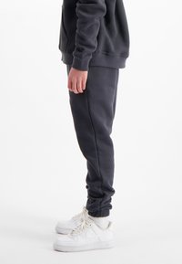 Donkergrijze sweatpants met een strakke boord bij de enkel, gecombineerd met witte sneakers. De stof lijkt zacht en ontspannen van vorm.