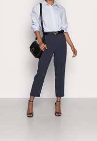 Ljusblå knäppt skjorta, marinblå skräddarsydda byxor, svart läderbälte med dubbel cirkulär spänne, svart handväska med gulddetalj och remsandaler.