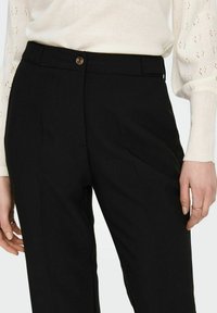 Pantalones negros de corte ajustado con una tela suave, que cuentan con un cierre frontal de botón, bolsillos laterales y un diseño de pliegue afilado.