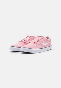 Par av låga rosa sneakers med vita sulor och vita Nike-swoosh-logotyper, visade i en vinkel på en vit bakgrund.