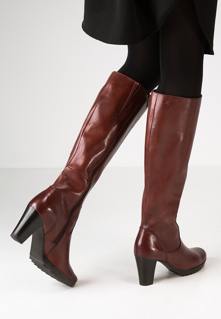 Botas altas de cuero marrón con un ajuste delgado, punta ligeramente redondeada y tacón de bloque. Cuenta con una cremallera lateral para facilitar su uso.