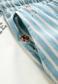 Světlomodrý a bílý pruhovaný materiál se silnou texturou; má vzor s kresleným psem a detailem s nařaseným pasem.