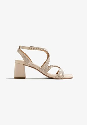 Sandale beige à bout ouvert avec des brides en cuir tressé, une boucle ajustable à la cheville et un talon bloc sur fond blanc.