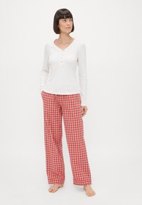 Wit katoenen top met lange mouwen, een V-hals en knoopdetails, gecombineerd met rode geruite pyjamabroek in een losse pasvorm.