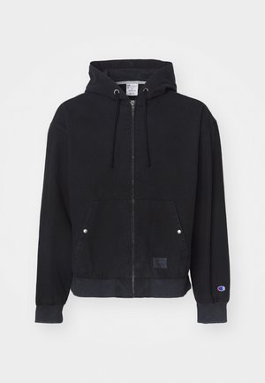 Czarna kurtka z kapturem na zamek wykonana z miękkiego materiału, z kieszenią kangurką, ściągaczami przy mankietach oraz małą metką z logo z przodu.