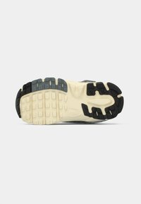 Suola di scarpa sportiva nera e grigia con battistrada in gomma testurizzata, caratterizzata da un intersuola spesso color crema e scanalature a motivi distinti per la trazione.