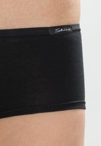 Czarne majtki typu boyshorts z elastycznego materiału, z płaskimi szwami i markowym paskiem w talii. Gładka tekstura, zaprojektowane z myślą o komforcie i dopasowaniu.