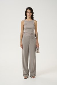 Débardeur gris à côtes avec épaules à clous, associé à un pantalon large gris clair, et un petit sac à main à motifs. Des sandales complètent le look.