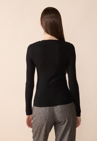 Svart långärmad topp med en åtsittande design och rund halsringning, tillverkad av ett smidigt, mjukt material. Buren med grå, strukturerade byxor.