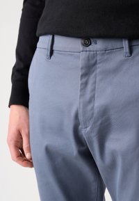 Pantalones azul claro hechos de una tela suave, con cierre de botón en la parte frontal y bolsillos laterales, usados con un suéter negro.