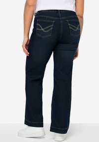 Tmavě modré džíny z denimu s bootcut nohavicemi, vybavené dvěma zadními kapsami se zdobným prošíváním a středním pasem. V kombinaci s bílými teniskami.