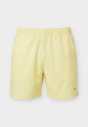 Bañador corto de hombre de color amarillo claro con cintura elástica y pequeño logo circular azul cerca del dobladillo inferior en la pierna derecha.