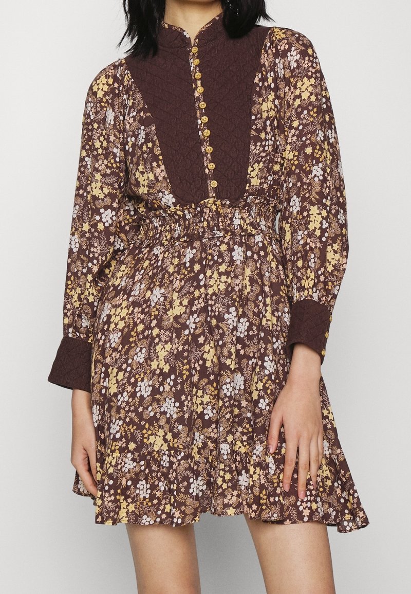 Robe fleurie marron avec des fleurs jaunes et blanches. Dotée d'un corsage texturé, d'une fermeture à boutons et d'un ourlet à volants. Manches longues avec poignets.