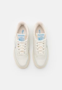 Baskets en cuir blanc avec des accents bleu clair, bout perforé et semelles de couleur crème. Les lacets sont bien disposés, mettant en valeur la marque sur la languette.