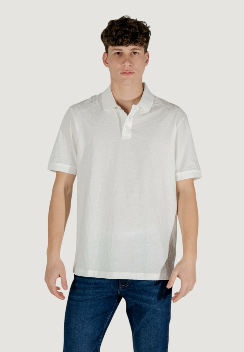 Polo bianco con un delicato motivo a trama, maniche corte e colletto classico. Abbinato a jeans blu.