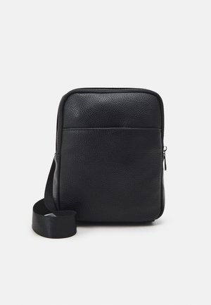 Sac messager en cuir noir avec une finition texturée, fermeture éclair, poche avant et une bandoulière réglable. Forme rectangulaire compacte.