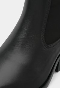 Černá kožená kotníková bota s hladkým povrchem, elastickými bočními panely a nízkým blokovým podpatkem. Důraz na minimalistický design a univerzálnost.