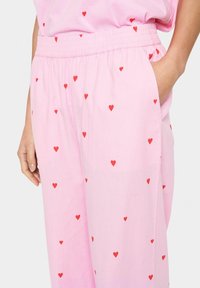 Lichtroze broek met verspreide kleine rode hartjespatronen, elastische tailleband, zijzakken en een losse, relaxte pasvorm.