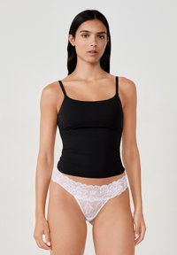 Top aderente nero con spalline sottili abbinato a perizoma bianco in pizzo con motivi floreali lungo la cintura. Texture liscia nel complesso.