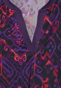 Tessuto a motivi viola e nero con vortici rossi e rosa. Il collo presenta un bordo viola solido con un design a forma di V.