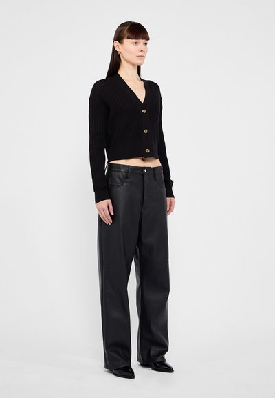 Cardigan noir court avec texture côtelée et boutons dorés, associé à un pantalon en cuir noir taille haute. Fini lisse et coupe décontractée.