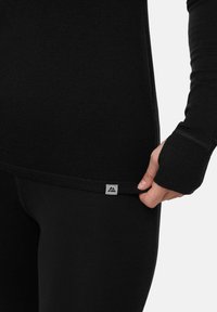 Haut noir à manches longues avec trous pour les pouces, texture lisse et étiquette de logo à l'ourlet. Design ajusté, tissu léger adapté au superposition.