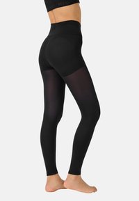 Schwarze Leggings aus dehnbarem Material mit einem hohen Bund und halbtransparenten Einsätzen an den Seiten, die für Komfort und Flexibilität konzipiert sind.