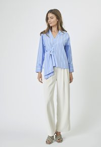 Light blue wrap blouse with vertical white stripes, long sleeves, and a front tie detail, paired with white wide-leg trousers.