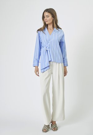 Light blue wrap blouse with vertical white stripes, long sleeves, and a front tie detail, paired with white wide-leg trousers.