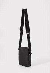 Black shoulder bag with a textured surface, rectangular shape, adjustable strap, and a zippered top closure. Simple design with minimal hardware.