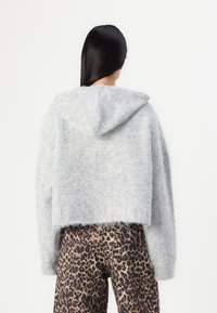 Grå huvtröja med fluffig textur, kort design och långa ärmar, kombinerad med byxor i leopardmönster.