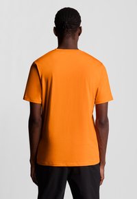 T-shirt di cotone arancione con maniche corte, colletto girocollo e texture liscia. Visto da dietro per mostrare il colore uniforme e il design semplice.