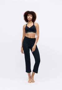 Soutien-gorge de sport noir avec un design en V et un logo de la marque ton sur ton sur la bande, associé à un pantalon cropped noir élastique. Tissu doux et extensible.