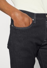 Černé džíny z denimu s viditelnými švy a předním kapsou. Látka působí pevně a hladce. Přiléhavý střih.