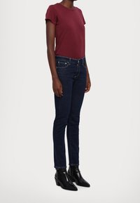 Camiseta burdeos de manga corta combinada con jeans de corte slim de color azul oscuro. Botines negros de tobillo con punta afilada y tacón grueso. Textura suave.