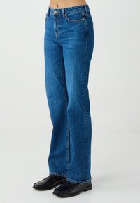 Blauwe denim jeans met een hoge taille, rechte pijpen, voorzakken en een sluiting met één knoop. De textuur is glad met minimale vervaging.