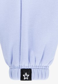 Hele sinine kootud kangast randmekate, millel on elastne tõmblukk ja must silt, millel on valge tähelogo. Sile tekstuur ja kujult vormitud.