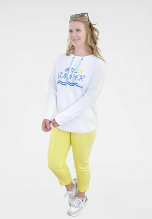 Weißer Kapuzenpullover mit blauem "Hello Summer"-Stick, kombiniert mit gelben, verkürzten Hosen und grauen Sneakers. Helles, lässiges Outfit.
