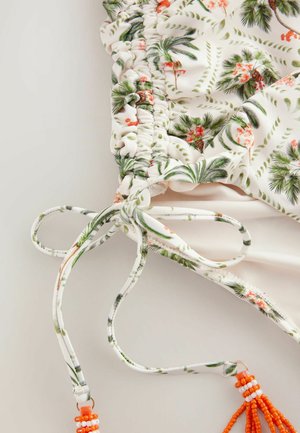 Top de bañador floral con base blanca y patrones de palmeras y flores verdes. Acabado con lazos ajustables y adornos de cuentas naranjas.