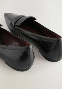 Schwarze Lederloafer mit Krokodilstruktur, spitzer Zehenform und flacher Sohle. Sie haben ein gespaltenes Riemendesign und ein glattes burgunderfarbenes Innenfutter.