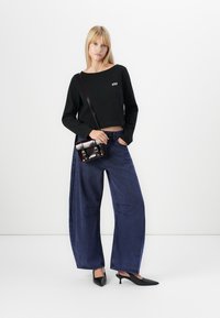 Black cropped sweatshirt with white logo, paired with wide-leg dark blue jeans featuring stitching details, and shiny black pointed-toe heels.