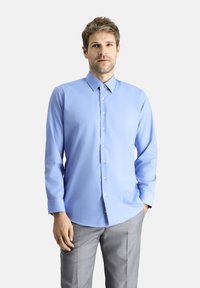 Camisa de manga larga azul claro con cuello abotonado, que presenta una textura suave y botones blancos, combinada con pantalones gris claro.