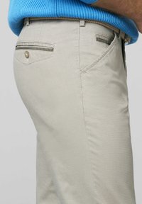 Helle beige Hose mit glatter Textur, ausgestattet mit einer einzelnen Gesäßtasche mit einem Knopf und einem grünen Akzentstreifen entlang der Tasche.
