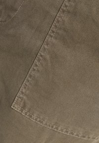 Bavlnená twill tkanina v tlumené olivově zelené barvě, s diagonálním vzorem stehu a přeloženým okrajem pro zvýšení textury.