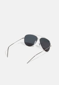 Ochelari de soare tip aviator din metal cu lentile întunecate, rame subțiri din argint și tampoane nazale din silicon transparent. Dispune de temple curbate pentru confort.