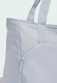 Bolso tote de color gris claro hecho de tela texturizada, con un bolsillo con cremallera, asas resistentes y una forma estructurada.