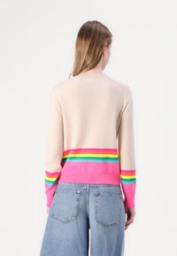 Beige genser laget av mykt materiale, med en rosa og flerfarget stripet kant og mansjetter. Oversized og avslappet passform, rund halsdesign.